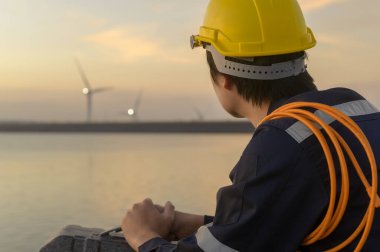 A male engineer wearing a protective helmet at sunset.	