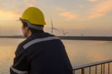 Günbatımında koruyucu kask takan bir erkek mühendis, arka plana özenle odaklanmış. 