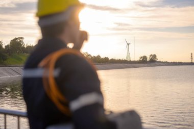 Günbatımında koruyucu kask takan bir erkek mühendis, arka plana özenle odaklanmış. 