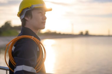 A male engineer wearing a protective helmet at sunset.	