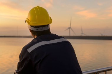 A male engineer wearing a protective helmet at sunset.	