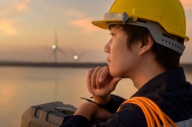 A male engineer wearing a protective helmet at sunset.	