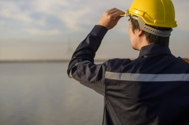 A male engineer wearing a protective helmet at sunset.	