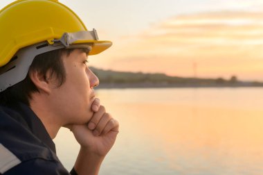 A male engineer wearing a protective helmet at sunset.	