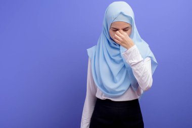 Başörtüsü takan genç Müslüman bir kadın mavi arka plan stüdyosu için stresli ve yorgun..