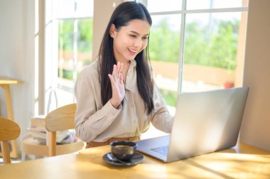 Kulaklıklı gülümseyen bir iş kadını laptopta webinar izliyor ve iş yerinde video görüşmesi yapıyor.