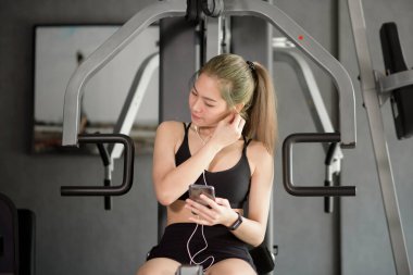 Sosyal ağ kullanan, spor salonunda müzik dinleyen, spor salonunda, spor salonunda ve teknoloji konseptinde gülümseyen güzel bir kadın.