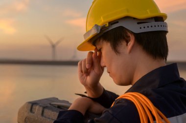 A male engineer wearing a protective helmet at sunset.	