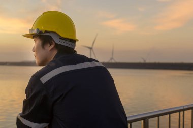 A male engineer wearing a protective helmet at sunset.	