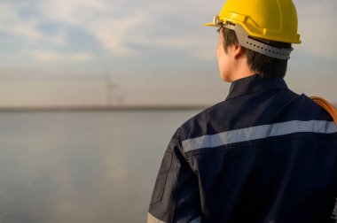 A male engineer wearing a protective helmet at sunset.	