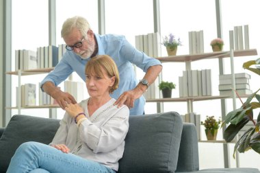 Kafkasyalı kıdemli adam oturma odasında karısına masaj yapıyor.