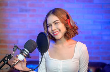 Renkli ışıklarla dolu bir müzik stüdyosunda şarkı söylerken mikrofonla kulaklık takan genç bir bayan şarkıcı..