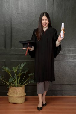 Mezuniyet elbisesi içinde siyah arka planda gülümseyen ve tezahürat yapan genç bir kadının portresi. 