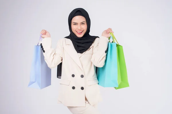 若いです美しいですイスラム教徒女性でスーツ保持カラフルなショッピングバッグ以上ホワイトバックスタジオ — ストック写真