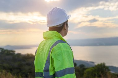 a man engineer is putting a protective helmet on her head at sunset.	