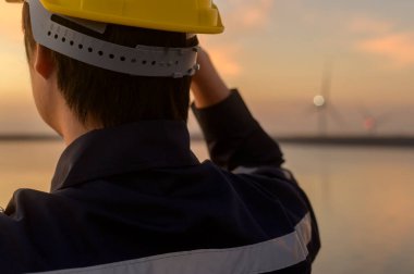A male engineer wearing a protective helmet at sunset.	