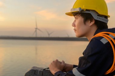 A male engineer wearing a protective helmet at sunset.	