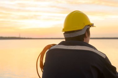A male engineer wearing a protective helmet at sunset.	