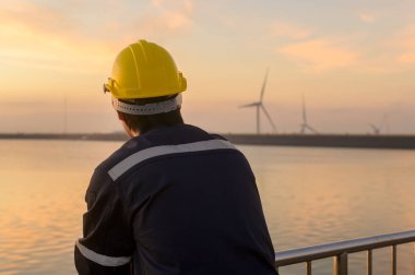 A male engineer wearing a protective helmet at sunset.	