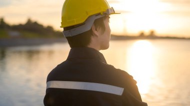 A male engineer wearing a protective helmet at sunset.	