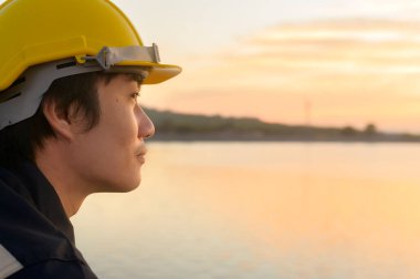 A male engineer wearing a protective helmet at sunset.	