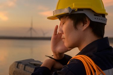 A male engineer wearing a protective helmet at sunset.	