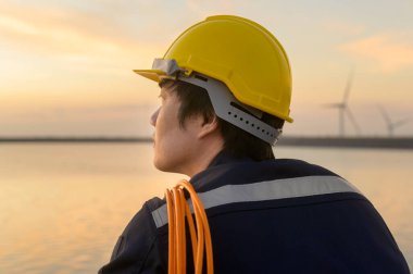 A male engineer wearing a protective helmet at sunset.	