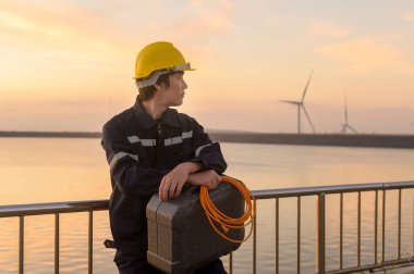 A male engineer wearing a protective helmet at sunset.	