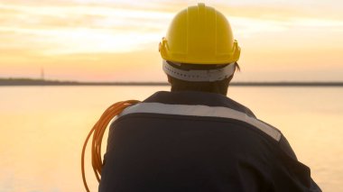 A male engineer wearing a protective helmet at sunset.	