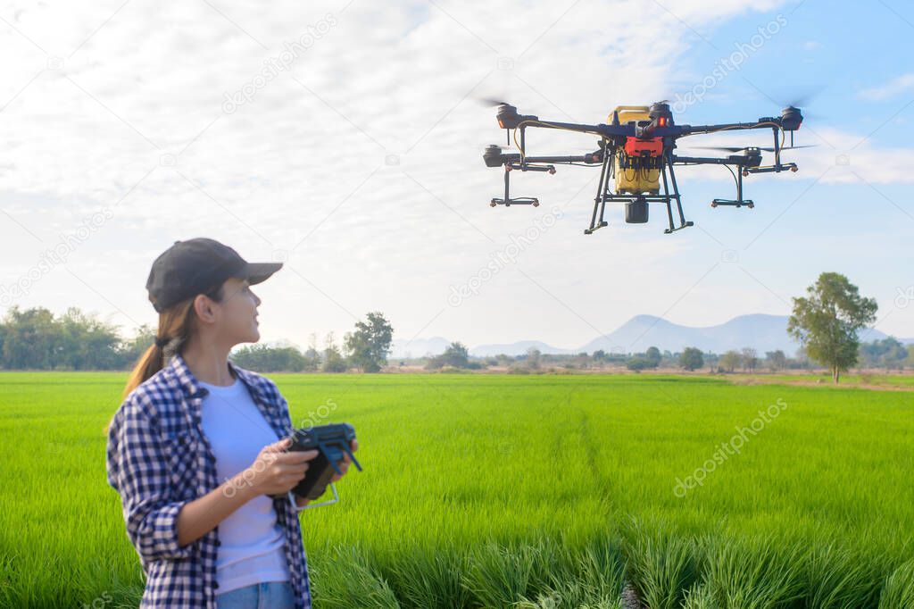 A young smart farmer controlling drone spraying fertilizer and pesticide over farmland,High technology innovations and smart farming