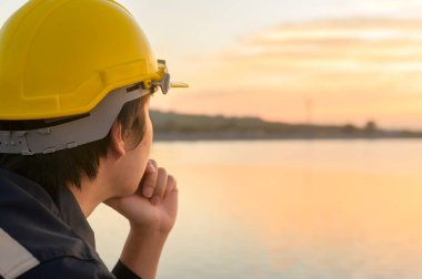 A male engineer wearing a protective helmet at sunset.	