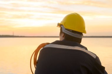 A male engineer wearing a protective helmet at sunset.	