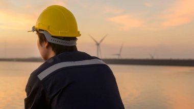 A male engineer wearing a protective helmet at sunset.	