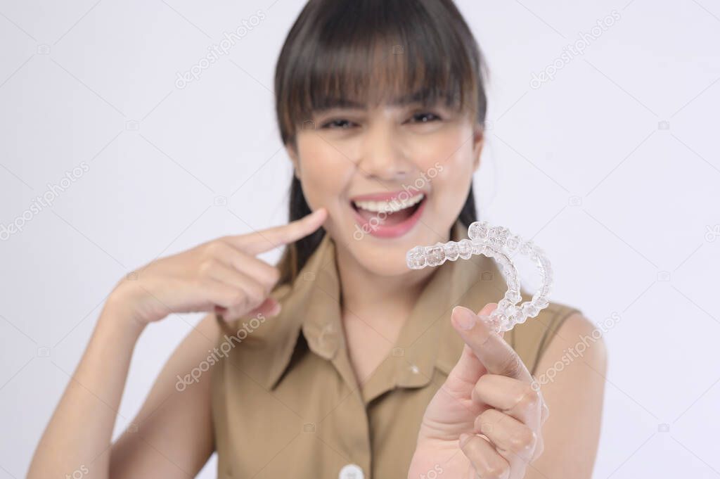 A young smiling woman holding invisalign braces over white background studio, dental healthcare and Orthodontic concept