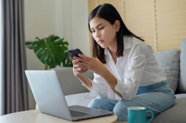 Genç ve mutlu bir kadın evde akıllı telefon, sosyal medya ve teknoloji kavramı kullanıyor..