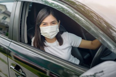 Koruyucu bir maske takan genç ve güzel bir kadın araba kullanıyor. 