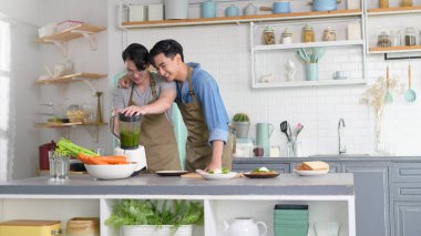 Genç, gülümseyen eşcinsel çift evde, mutfakta meyve suyu makinesiyle meyve suyu yapıyor, LGBTQ ve çeşitlilik konsepti.