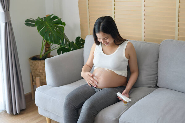 Young pregnant woman applying moisturizing cream on tummy, healthcare and pregnancy care