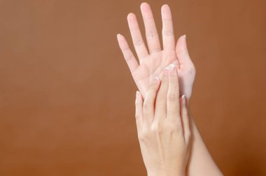 Yakın plan genç kadın eli kahverengi arka plan üzerine krem sürüyor, güzellik ve cilt bakımı kavramı. 