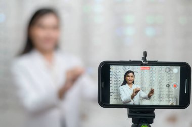 A Young ophthalmologist doing live streaming via smart phone present new collection of glasses in optical center, eyecare concept.