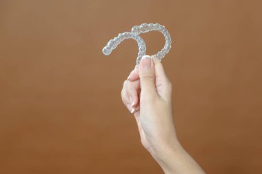 Yakın plan genç kadın eli Invisalign 'i kahverengi arka plan üzerinde tutuyor. 