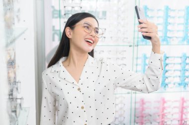 Genç bir bayan müşteri gözlük deniyor ve optik merkezde selfie çekiyor, Eyecare konsepti..