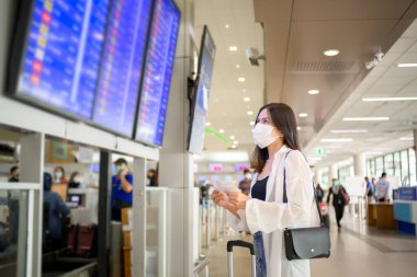 A traveller woman is wearing protective mask in International airport, travel under Covid-19 pandemic, safety travels, social distancing protocol, New normal travel concept .	