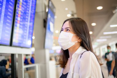 A traveller woman is wearing protective mask in International airport, travel under Covid-19 pandemic, safety travels, social distancing protocol, New normal travel concept .	