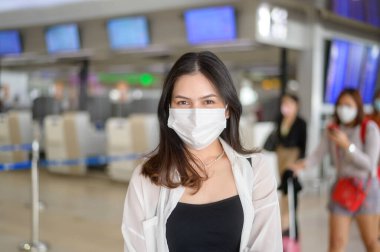 A traveller woman is wearing protective mask in International airport, travel under Covid-19 pandemic, safety travels, social distancing protocol, New normal travel concept .	