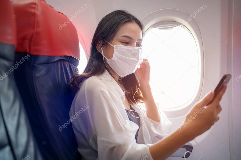 A Young woman wearing face mask is using smartphone onboard, New normal travel after covid-19 pandemic concept