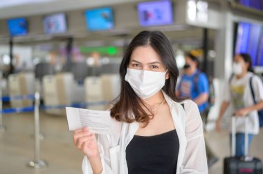 A traveller woman is wearing protective mask in International airport, travel under Covid-19 pandemic, safety travels, social distancing protocol, New normal travel concept .	