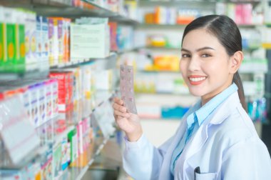 A Female pharmacist wearing lab coat in a modern pharmacy drugstore., selecting a medicine for customer.	