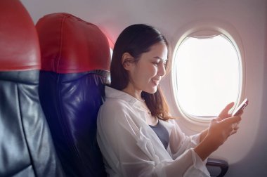 Genç ve güzel bir kadın uçakta, seyahatte ve tatillerde akıllı telefon kullanıyor.