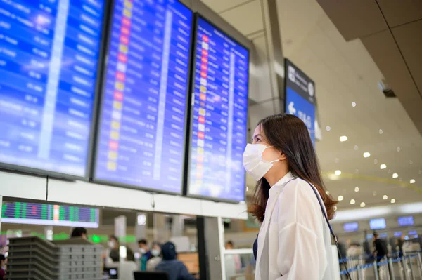 A traveller woman is wearing protective mask in International airport, travel under Covid-19 pandemic, safety travels, social distancing protocol, New normal travel concept .